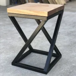 Nowoczesny stolik pomocniczy z blatem z jasnego drewna i geometryczną podstawą z czarnego metalu, na szarym betonowym tle.