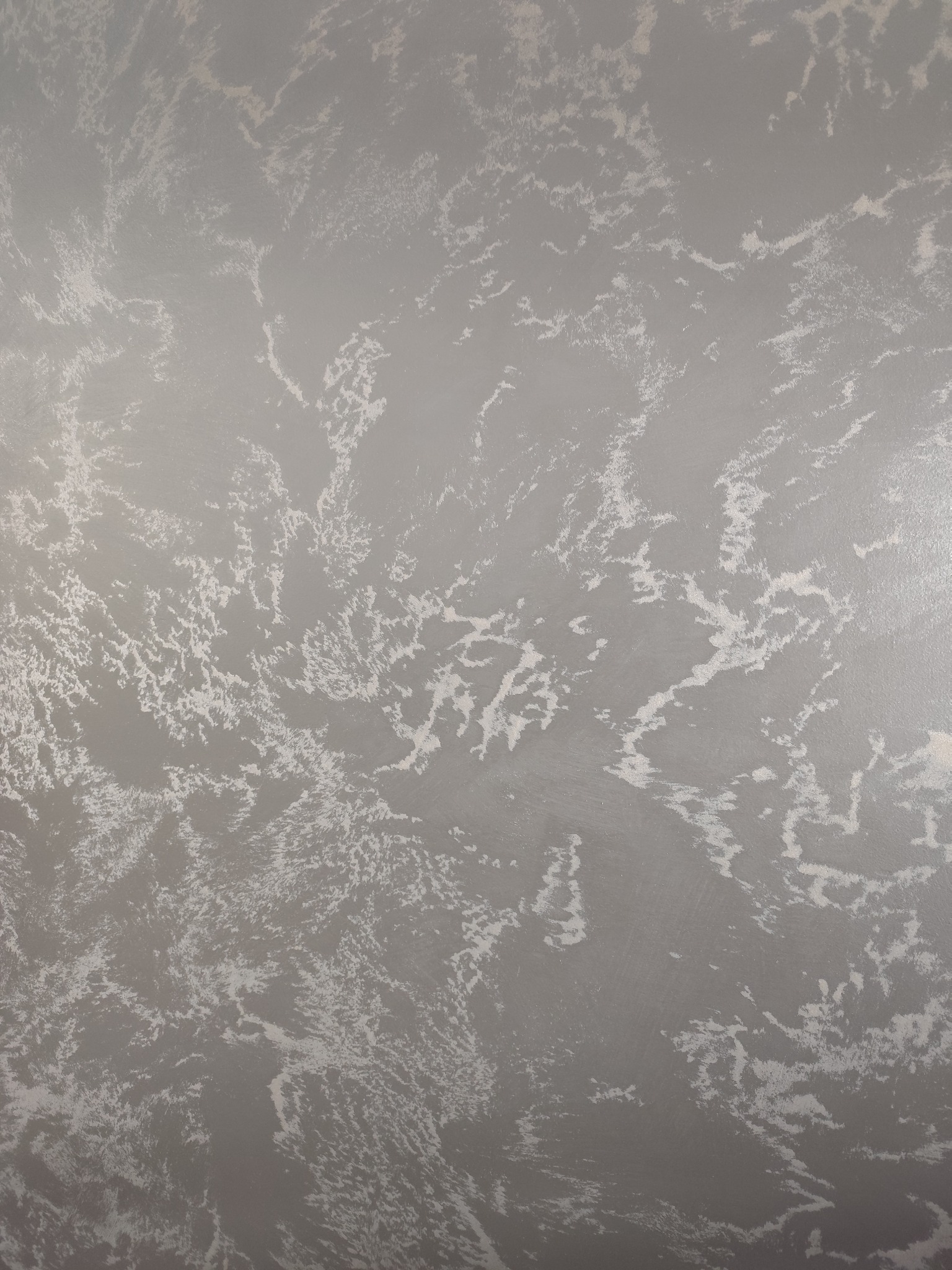 Szara ściana z dekoracyjną, nieregularną fakturą w odcieniach bieli i szarości, przypominająca marmurkowy wzór. Gładka powierzchnia z delikatnym połyskiem.