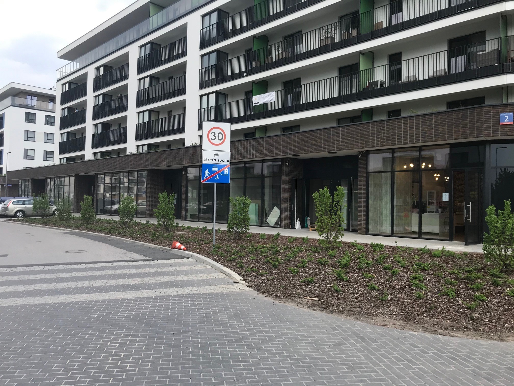 Nowoczesny budynek wielorodzinny z balkonami i lokalami usługowymi na parterze, widoczne duże przeszklenia.