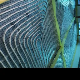 Wewnętrzny widok instalacji ogrzewania podłogowego z rurkami ułożonymi w pętle na folii z siatką, przyklejonej taśmą do ściany.