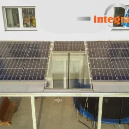 Fotowoltaika zintegrowana z zadaszeniem tarasu, widok z góry na panele słoneczne na białej konstrukcji, w tle ogród i dom, logo firmy Integral Energia z Natury w prawym górnym rogu.