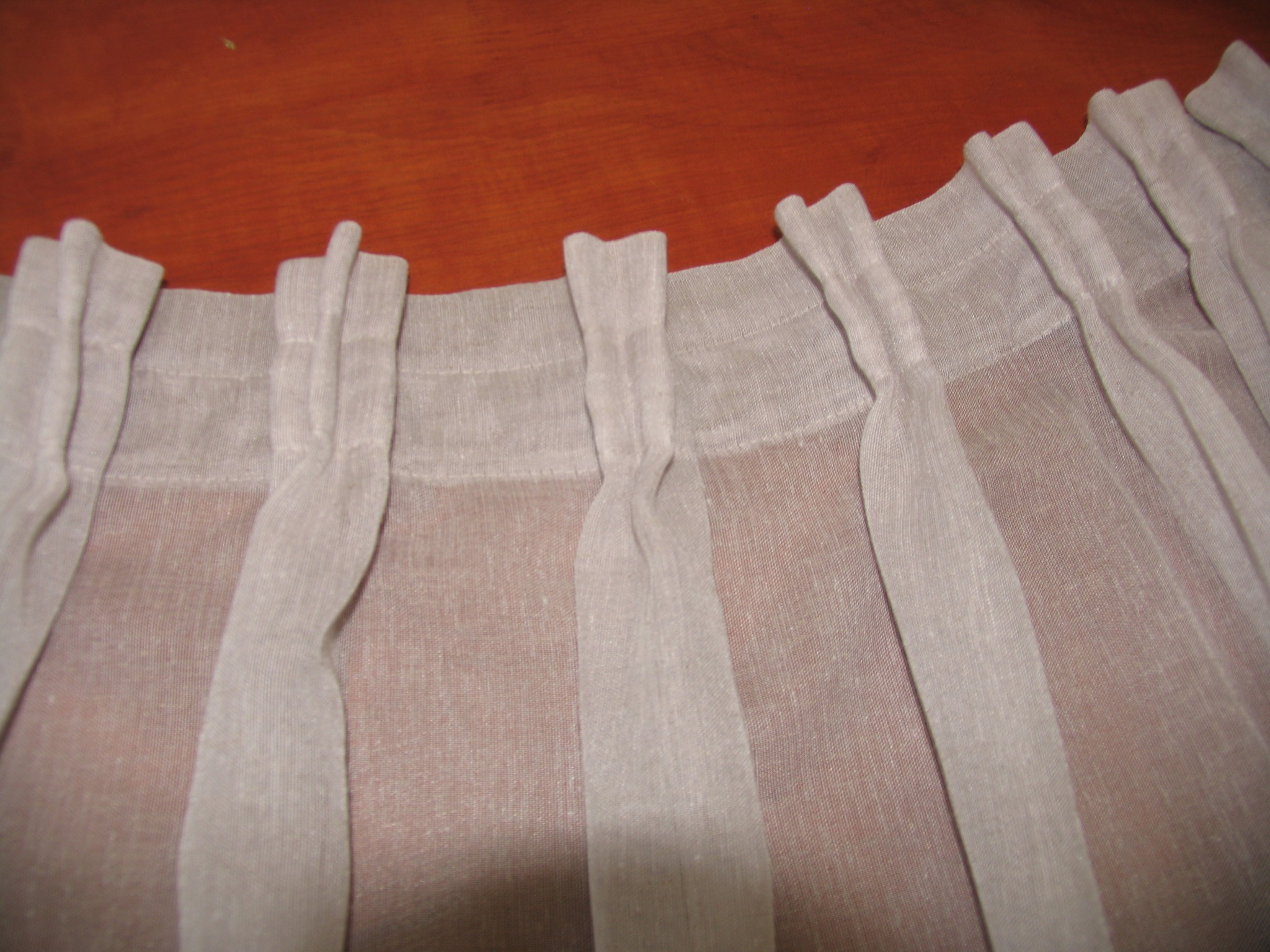 Jasnoszara, lniana zasłona z marszczeniami na taśmie, zbliżenie na górną krawędź i szlufki, widoczne delikatne prześwity materiału.