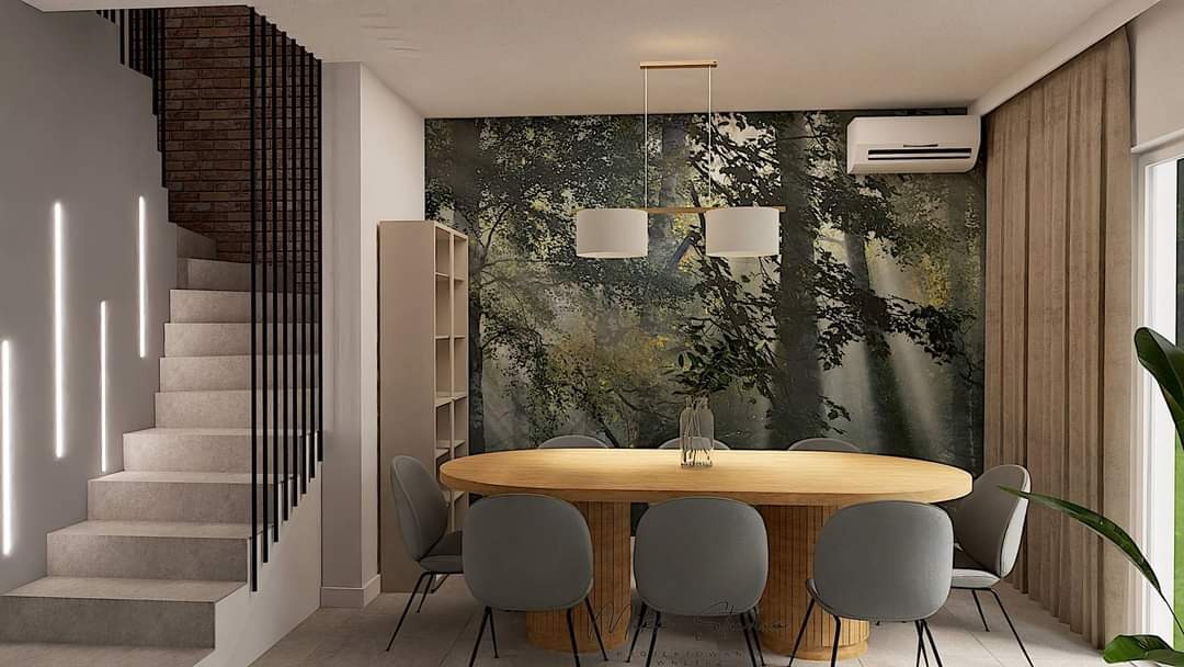 Jadalnia z owalnym stołem z drewnianym blatem i szarymi krzesłami na tle tapety z motywem leśnym, oświetlona lampami wiszącymi i światłem schodowym.