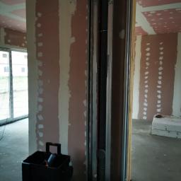 SandroSolution - Wnętrze w trakcie prac wykończeniowych: ściany z płyt gipsowo-kartonowych z widocznymi śladami szpachlowania, pionowa konstrukcja z profili metalowych i drewnianych, prawdopodobnie obudowa...
