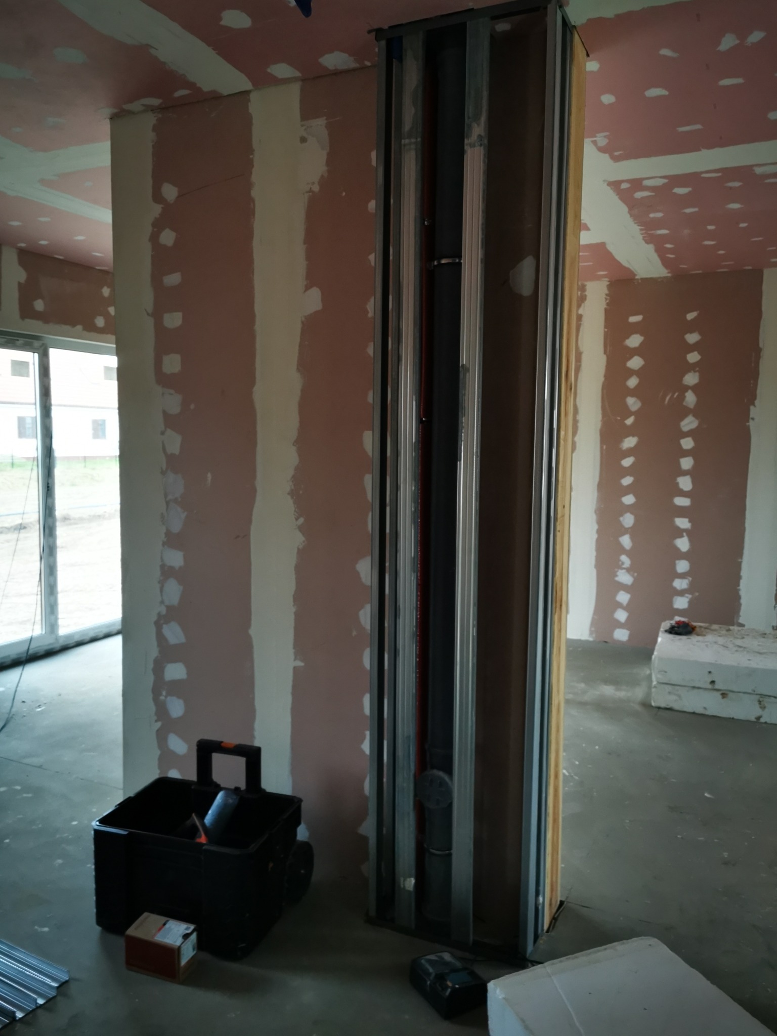 Wnętrze w trakcie prac wykończeniowych: ściany z płyt gipsowo-kartonowych z widocznymi śladami szpachlowania, pionowa konstrukcja z profili metalowych i drewnianych, prawdopodobnie obudowa...