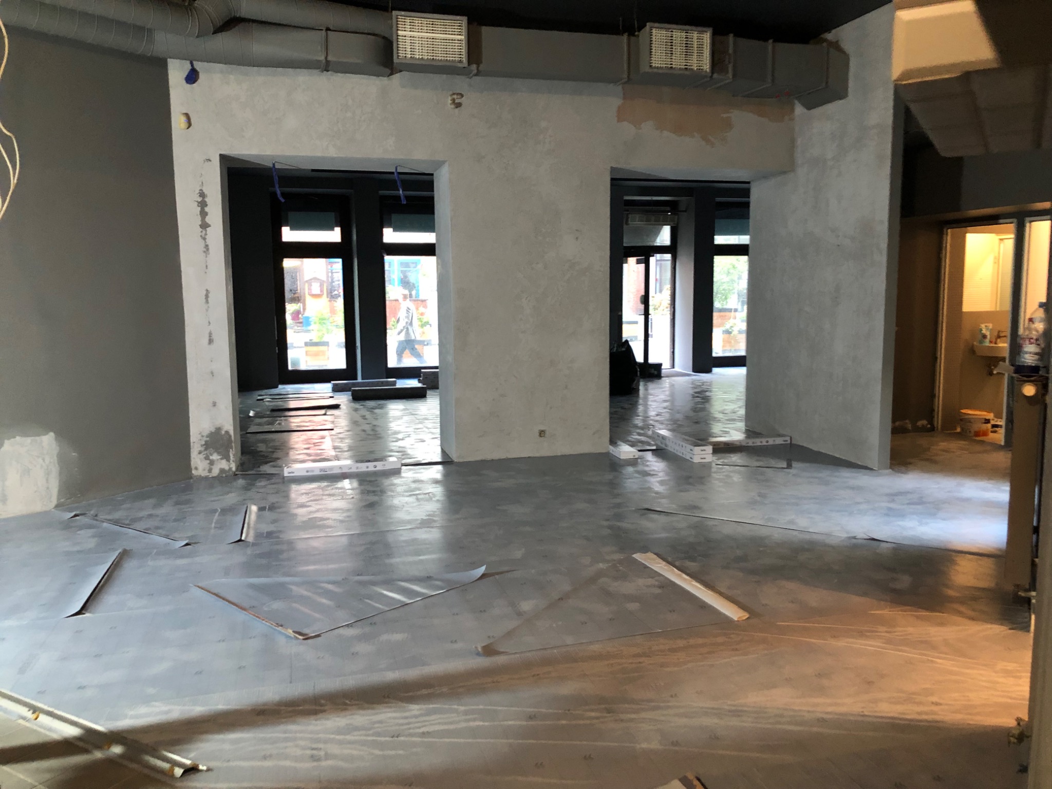 Przygotowanie podłoża pod nową posadzkę w lokalu usługowym, widoczne zabezpieczone folią podłoże i profile dylatacyjne w progach drzwiowych.