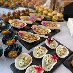 Pinchos_wroclaw - Różnorodne przekąski na czarnych deskach i białym obrusie: mini burgery, sałatki w łódeczkach z drewna i ryżu, kulki mięsne, dekorowane kwiatami.