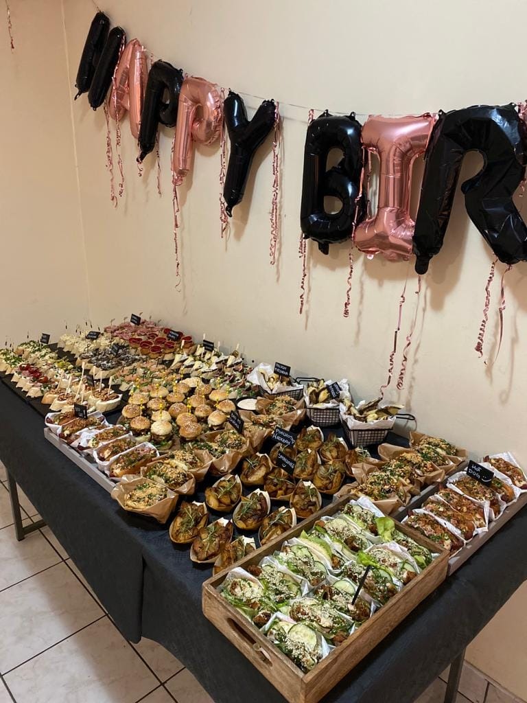 Stół z różnorodnymi przekąskami cateringowymi, w tle balony z napisem 'HAPPY BIRTHDAY'