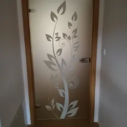 Szklane drzwi wewnętrzne z drewnianą ramą i dekoracyjnym motywem roślinnym z matowego szkła.
