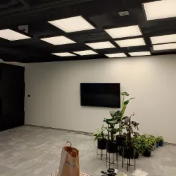 Biuro po montażu oświetlenia sufitowego LED, widoczne rośliny doniczkowe, telewizor na ścianie i gaśnica.