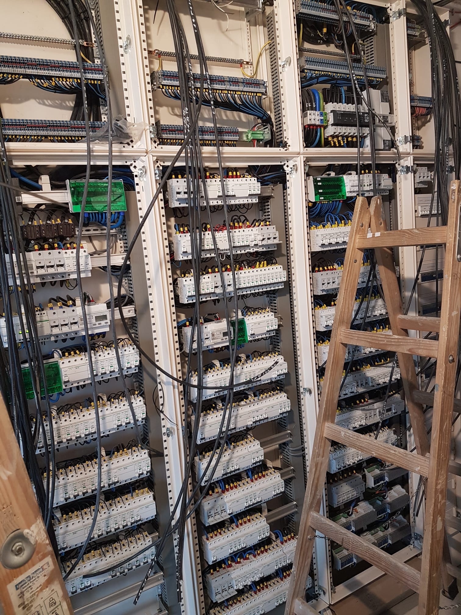 Rozbudowana rozdzielnica elektryczna z licznymi zabezpieczeniami i okablowaniem, widoczna drabina monterska.