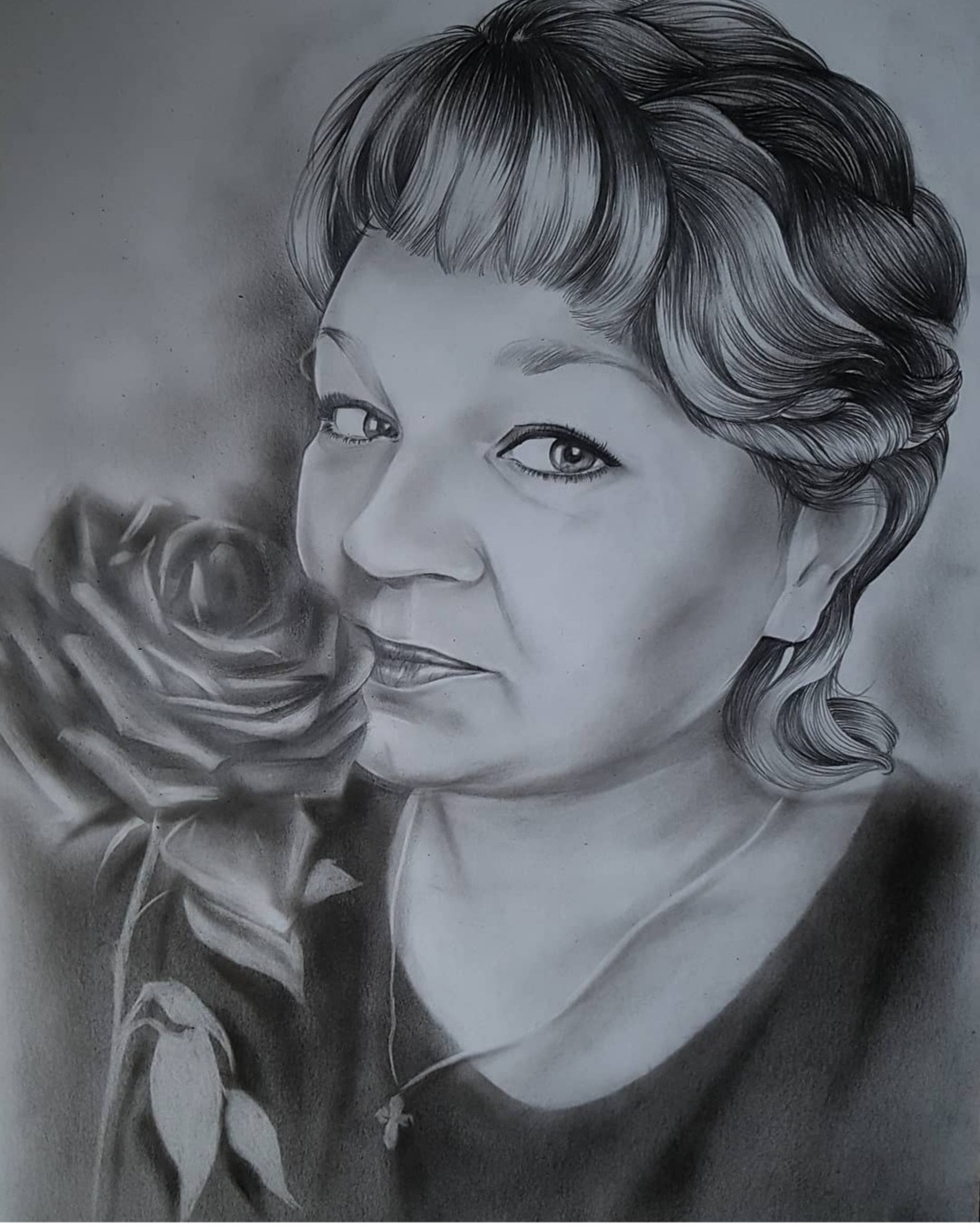 Szkic ołówkiem przedstawiający portret kobiety z różą, widoczny delikatny łańcuszek z krzyżykiem na szyi.