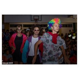 Kacper Polaczyk - Młodzież w barwnych strojach i perukach, prawdopodobnie podczas szkolnego przedstawienia lub imprezy tematycznej, na tle widowni i boiska do koszykówki.