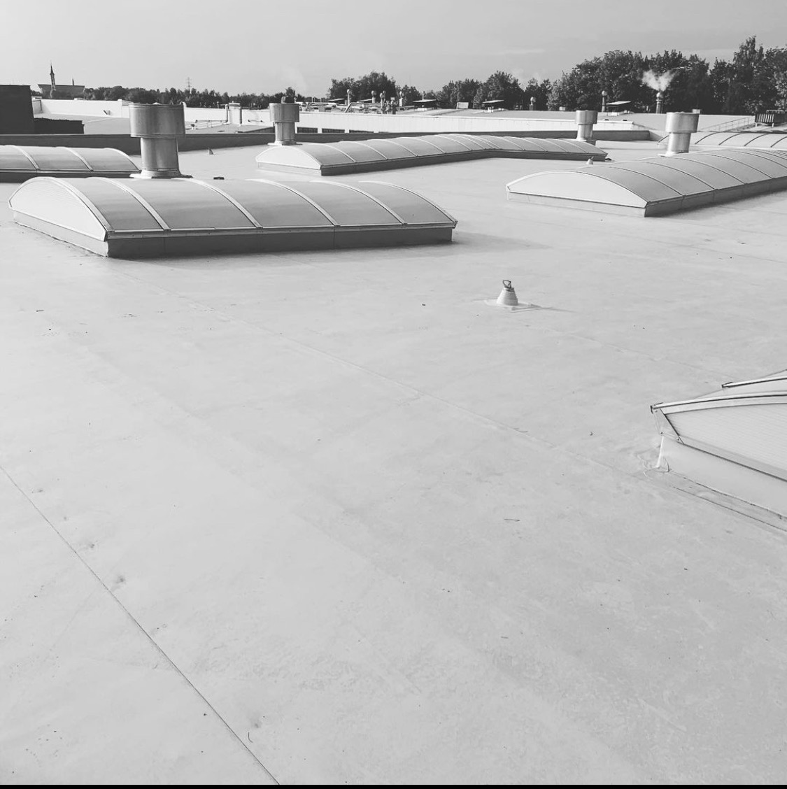 Czarno-białe zdjęcie płaskiego dachu przemysłowego z świetlikami kopułowymi i kominami wentylacyjnymi.