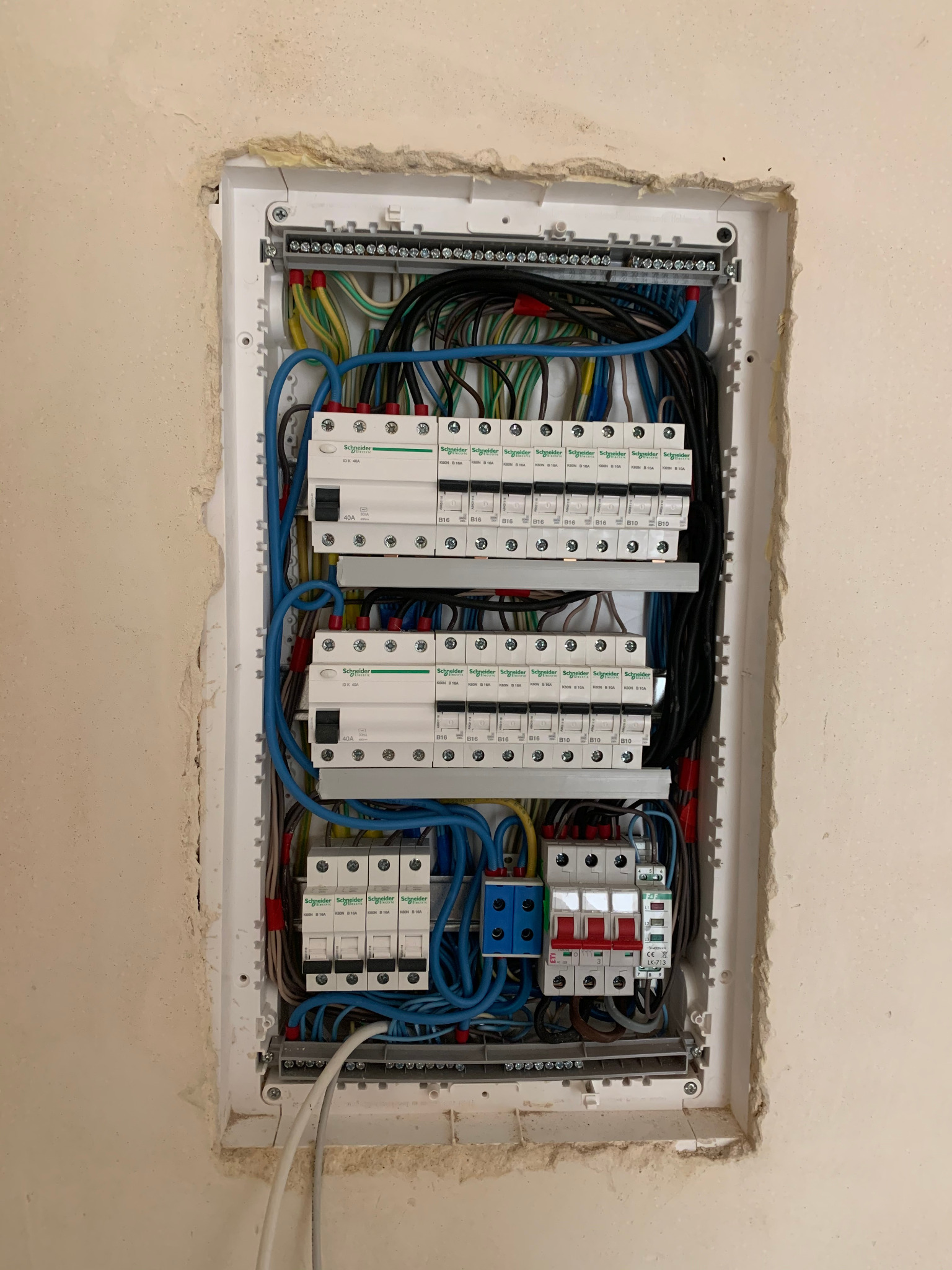 Wnętrze rozdzielnicy elektrycznej Schneider zamontowanej w ścianie, widoczne przewody, bezpieczniki i wyłączniki, ściana wokół rozdzielnicy wymaga wykończenia.