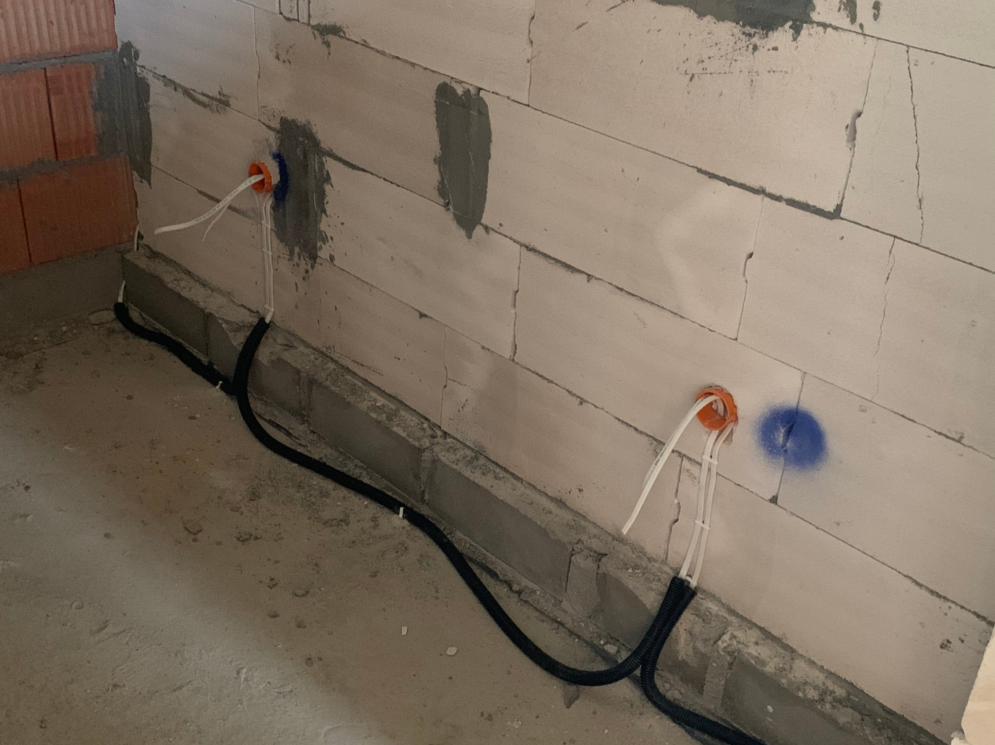 Rozprowadzenie przewodów elektrycznych w karbowanej rurze, wychodzących z pomarańczowych puszek instalacyjnych w surowym stanie budynku z betonowych bloczków.