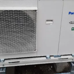 Zewnętrzna jednostka klimatyzacji Panasonic Inverter R32 na metalowej konstrukcji, widoczne ślady deszczu na obudowie.