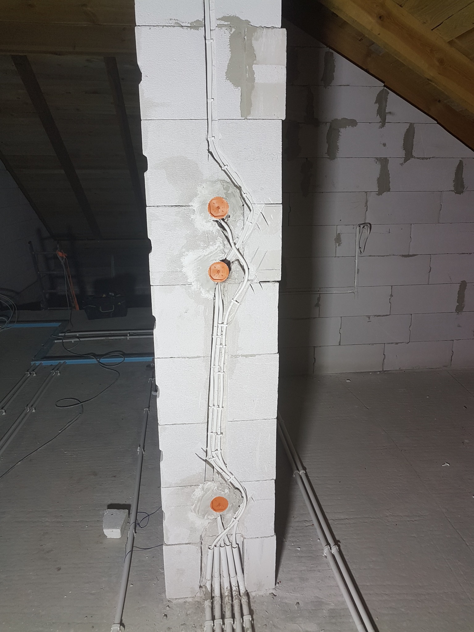 Ściana z betonu komórkowego w trakcie montażu instalacji elektrycznej: widoczne przewody, puszki instalacyjne i fragment drewnianej konstrukcji dachu na poddaszu.