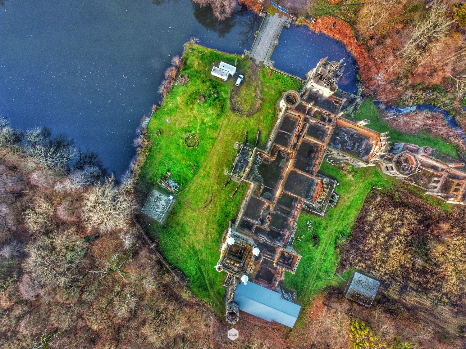 Widok z drona na ruiny zamku położonego nad jeziorem, otoczonego zielenią i lasem.