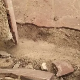 Fragment zdemontowanej, czerwonej, ceramicznej podłogi z widocznymi resztkami zaprawy i gruzu.