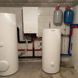 Instalacja centralnego ogrzewania Viessmann z dwoma zasobnikami ciepłej wody i kotłem gazowym kondensacyjnym w kotłowni wyłożonej białymi płytkami.