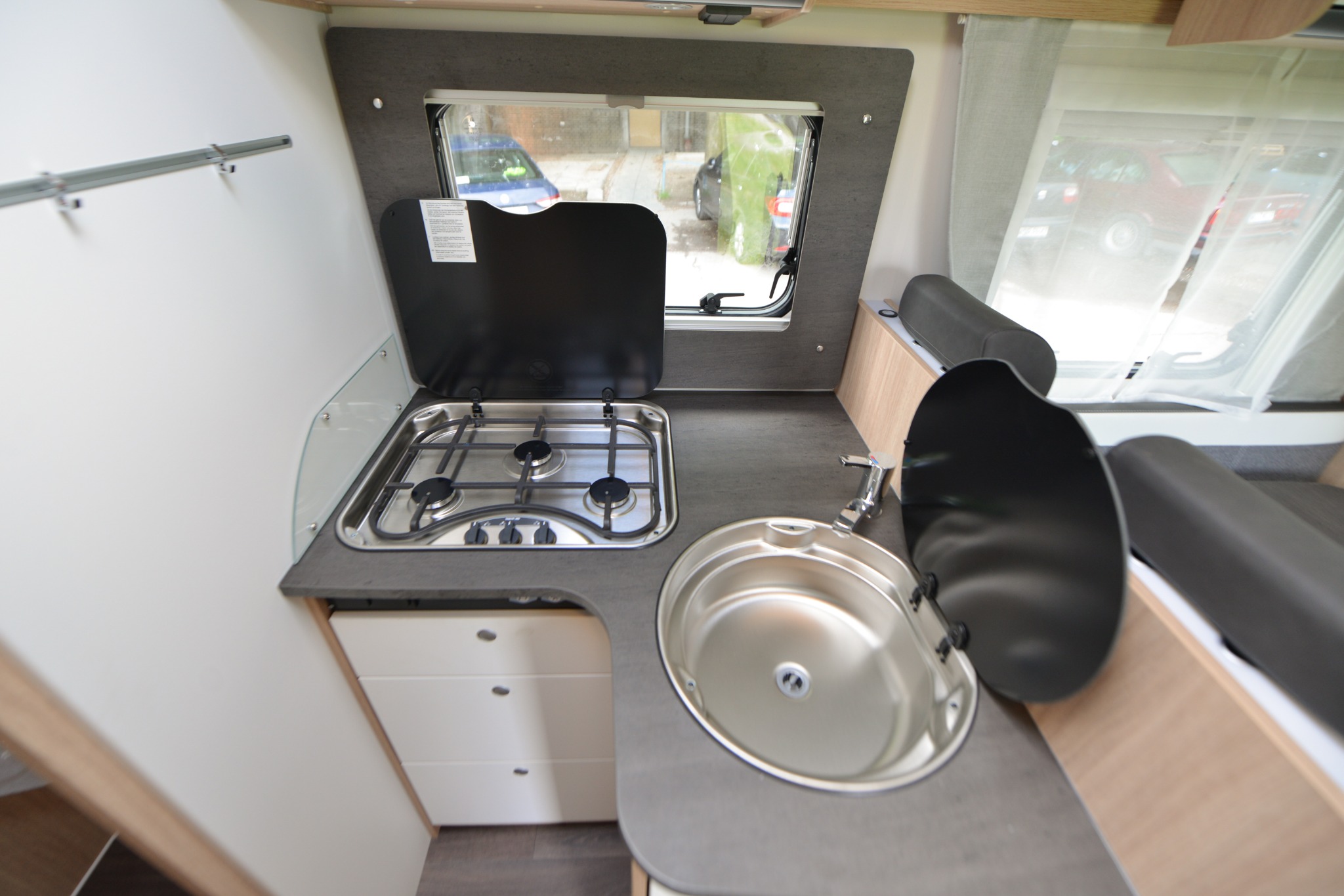 Wnętrze kampera z kuchenką gazową, zlewozmywakiem i oknem z widokiem na ulicę.