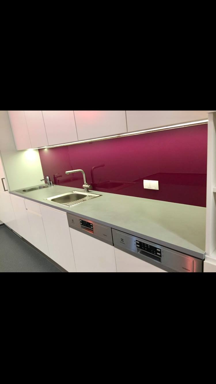 Nowoczesna kuchnia z białymi szafkami, szarym blatem i bordowym panelem szklanym nad zlewem, uzupełniona oświetleniem podszafkowym i srebrną zmywarką.