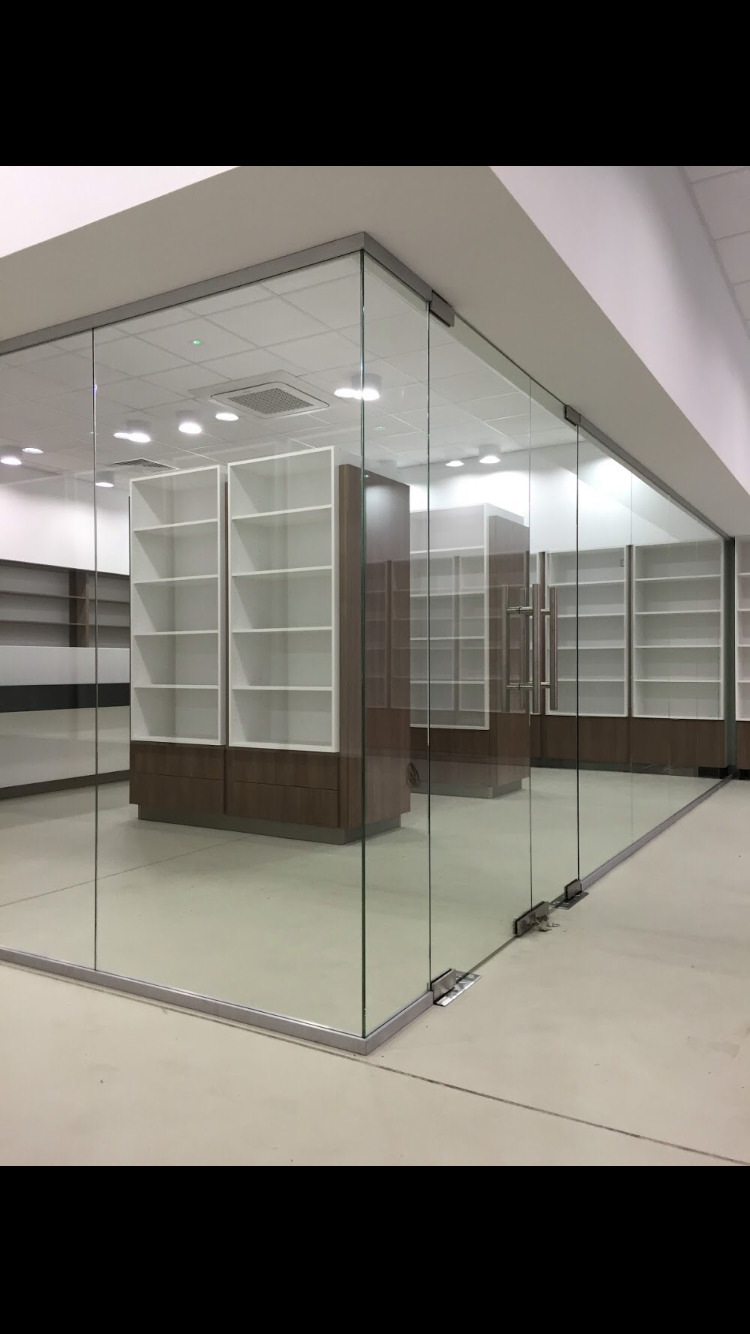 Szklana ścianka działowa z aluminiowymi profilami, oddzielająca przestrzeń biurową z widocznymi regałami na dokumenty, w jasnym, minimalistycznym wnętrzu.