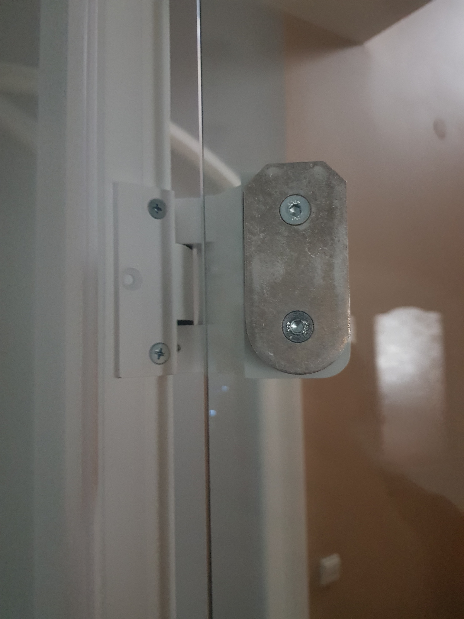 Szczegółowe ujęcie zawiasu mocującego szklane drzwi kabiny prysznicowej, widoczne śruby mocujące i elementy konstrukcyjne.