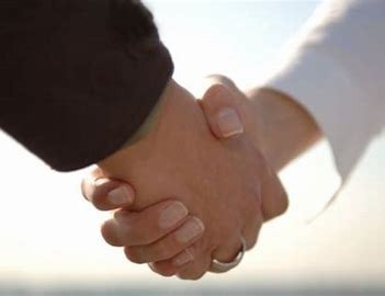 Uścisk dłoni dwóch osób, jedna w ciemnym garniturze, druga w białej koszuli, symbolizujący zawarcie umowy lub partnerstwo, z delikatnym rozmyciem tła.