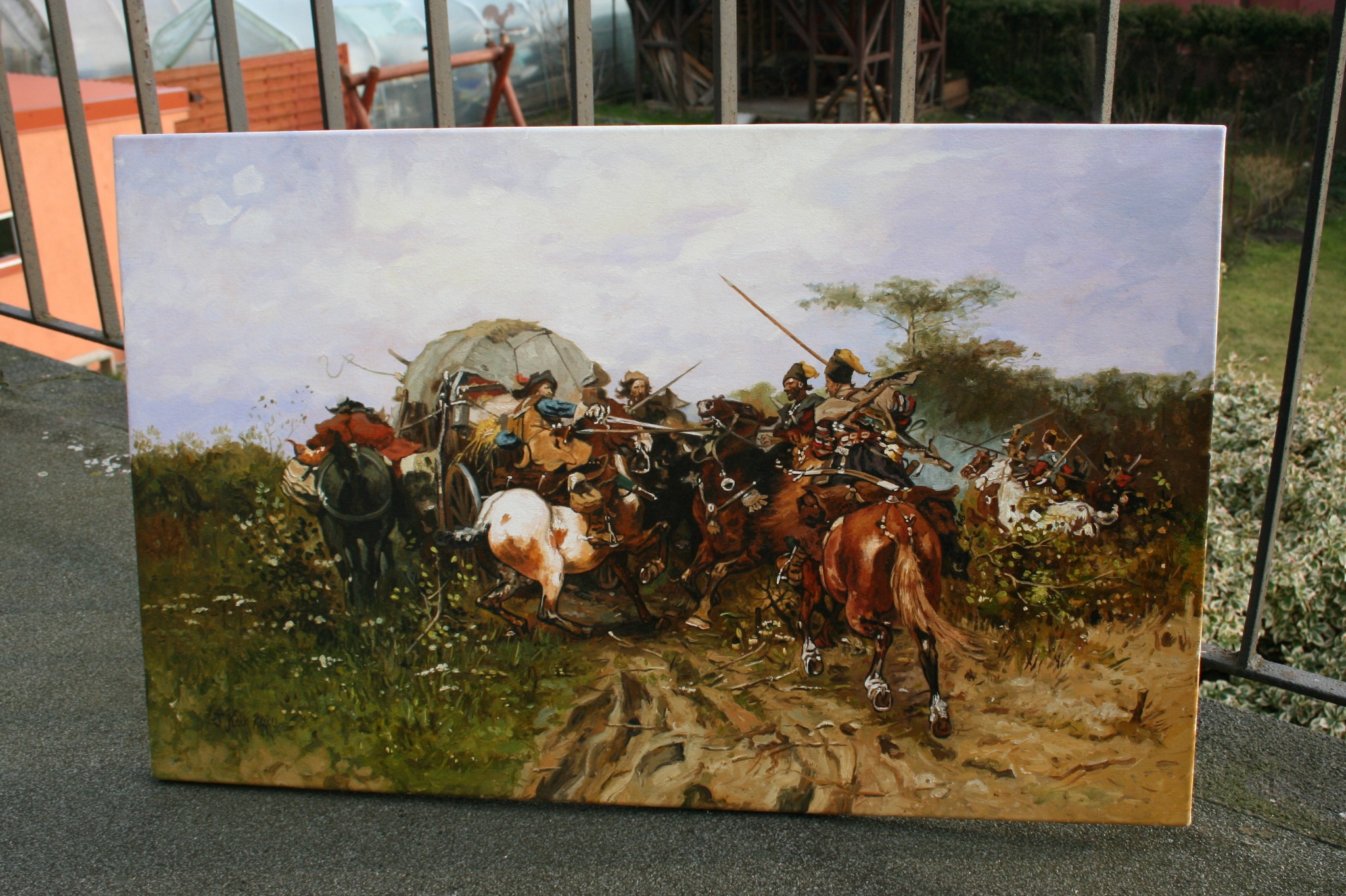 Obraz olejny przedstawiający dynamiczną scenę bitewną z jeźdźcami na koniach i wozem, umieszczony na zewnątrz na betonowym murku z widoczną zielenią w tle.