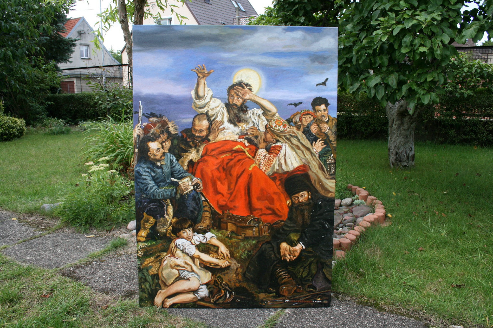 Duży obraz przedstawiający scenę historyczną z postaciami w strojach z epoki, umieszczony na trawniku przed domem z ogrodem.