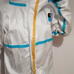 Biały kombinezon ochronny z niebieskimi i żółtymi paskami, założona niebieska rękawica, widoczny emblemat producenta na ramieniu.