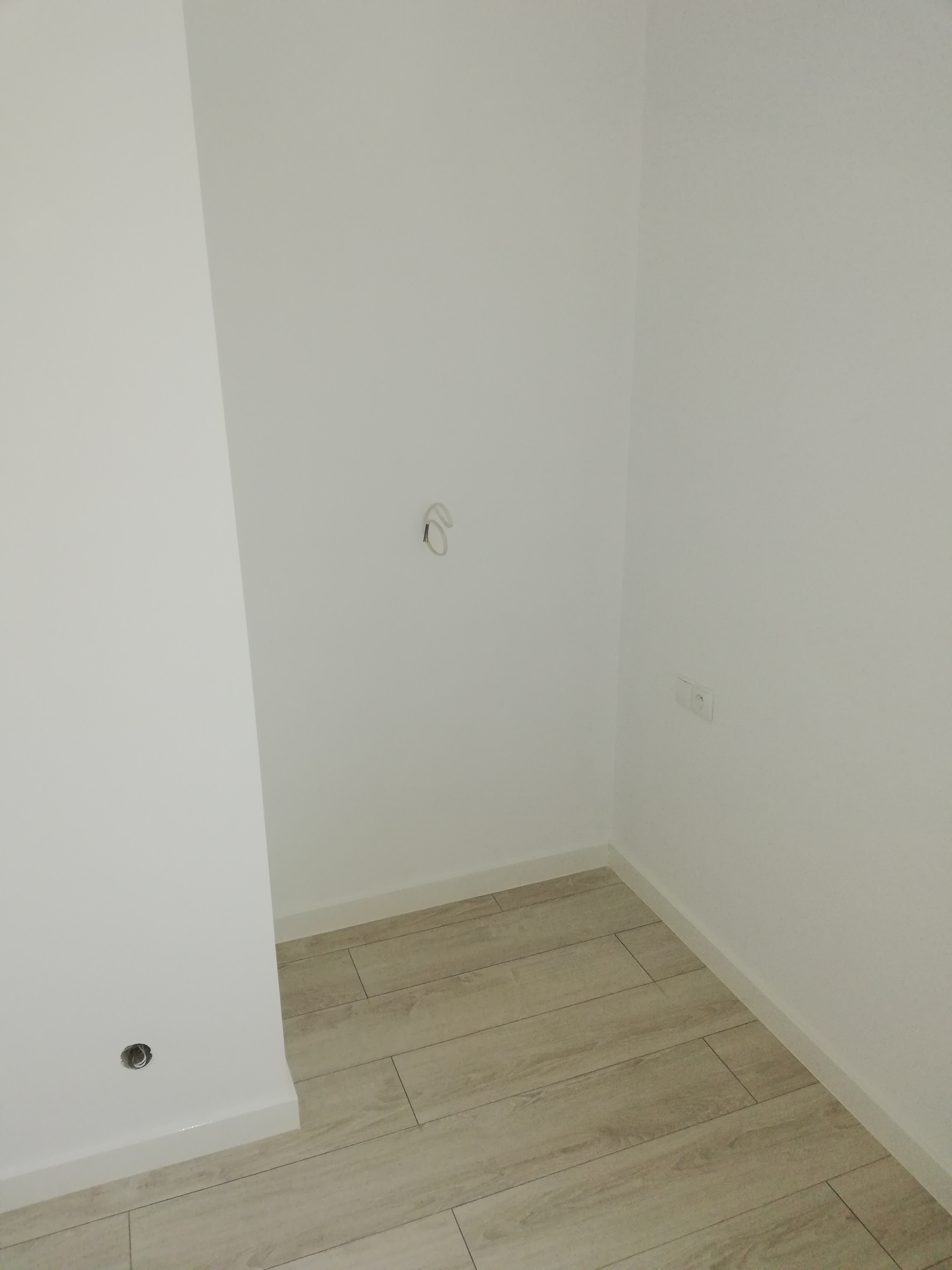 Wnętrze po remoncie: ściany pomalowane na biało, położona jasna podłoga imitująca drewno, widoczne gniazdko elektryczne i wyprowadzone przewody.