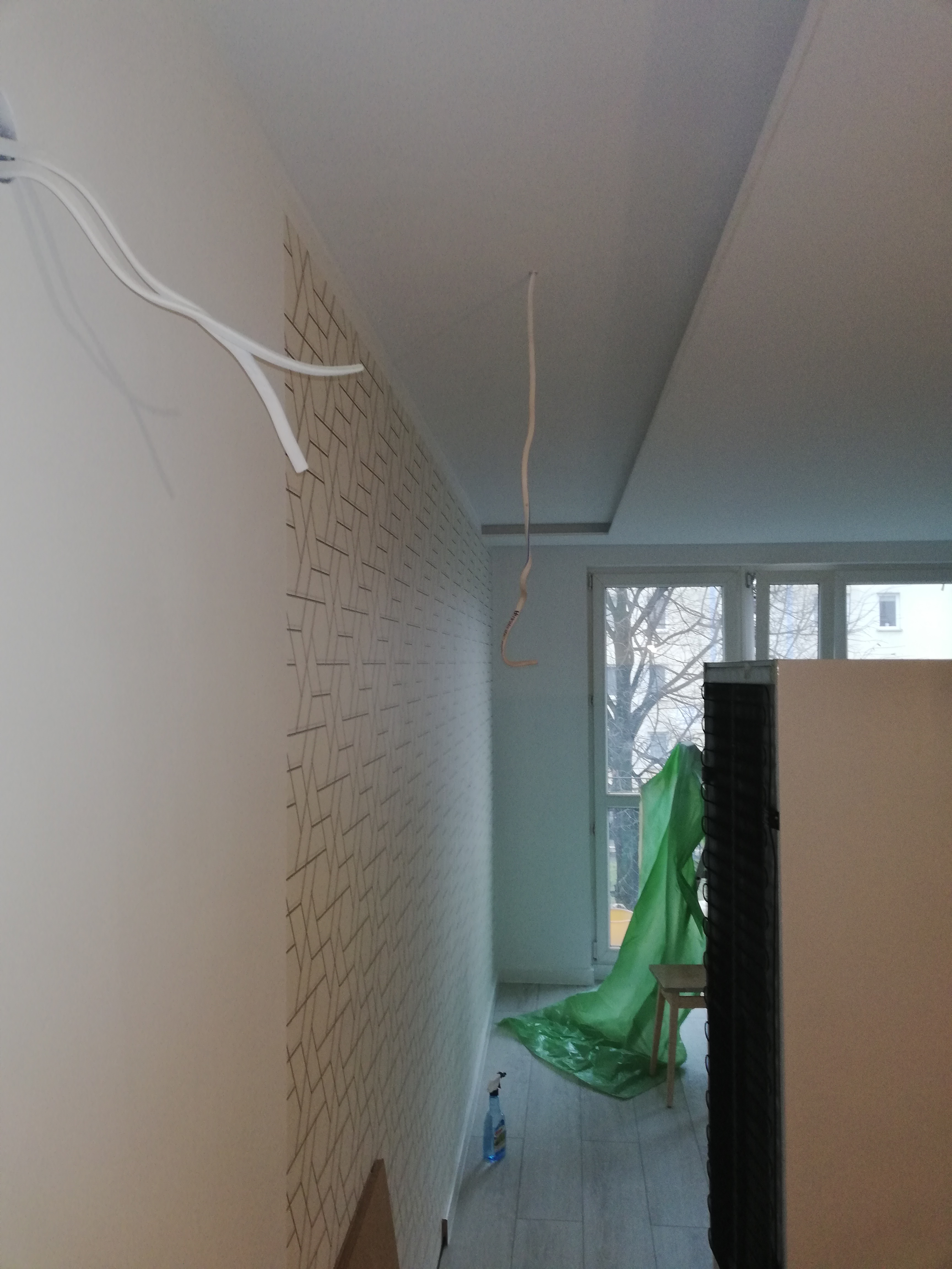 Remontowane wnętrze: ściana z tapetą w geometryczne wzory, widoczne kable elektryczne i zabezpieczona folią podłoga, sugerujące prace wykończeniowe.