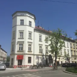 Kamienica w Krakowie z białą elewacją, narożna wieżyczka, przed budynkiem rowerzysta i ogródek restauracyjny, widoczna drabina przy wejściu do lokalu Well Done.