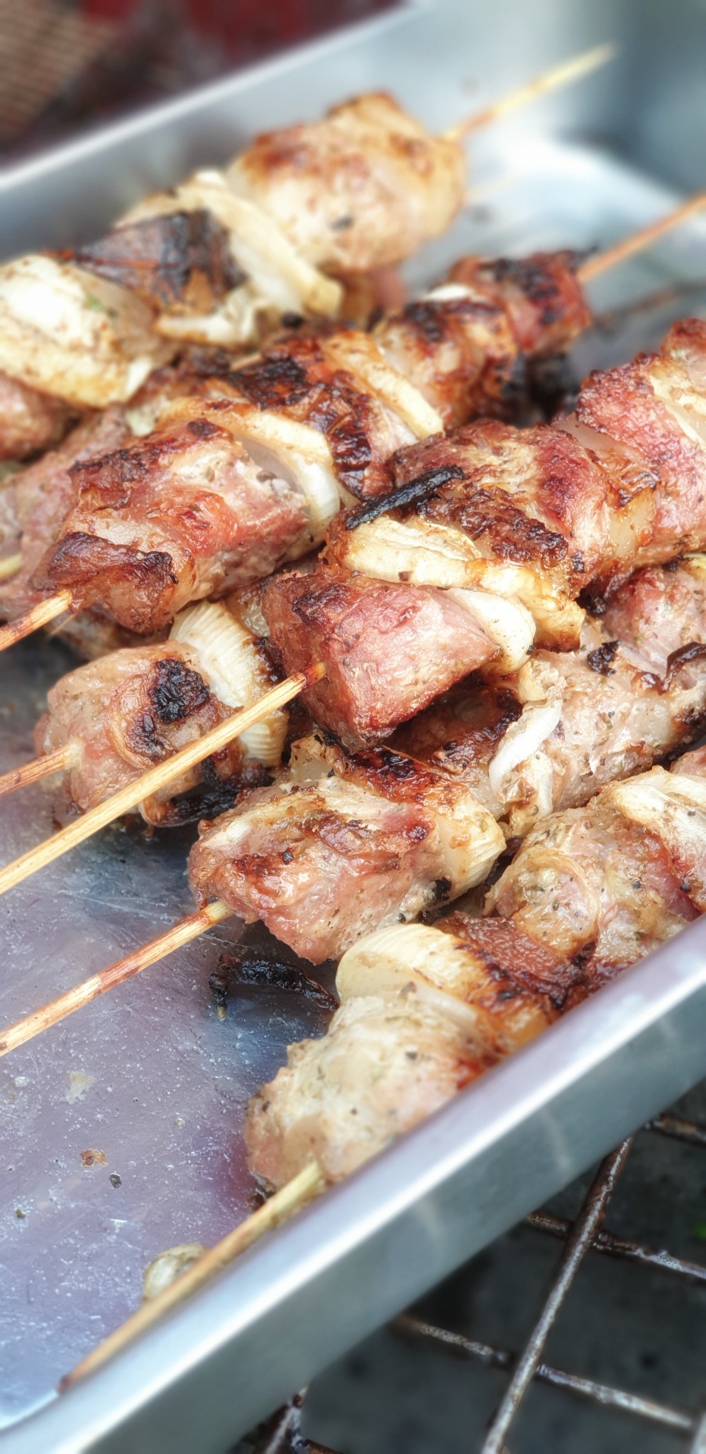 Szpikulce z grillowanym mięsem i cebulą, ułożone na metalowej tacy, widoczne ślady przypalenia, oświetlenie dzienne.