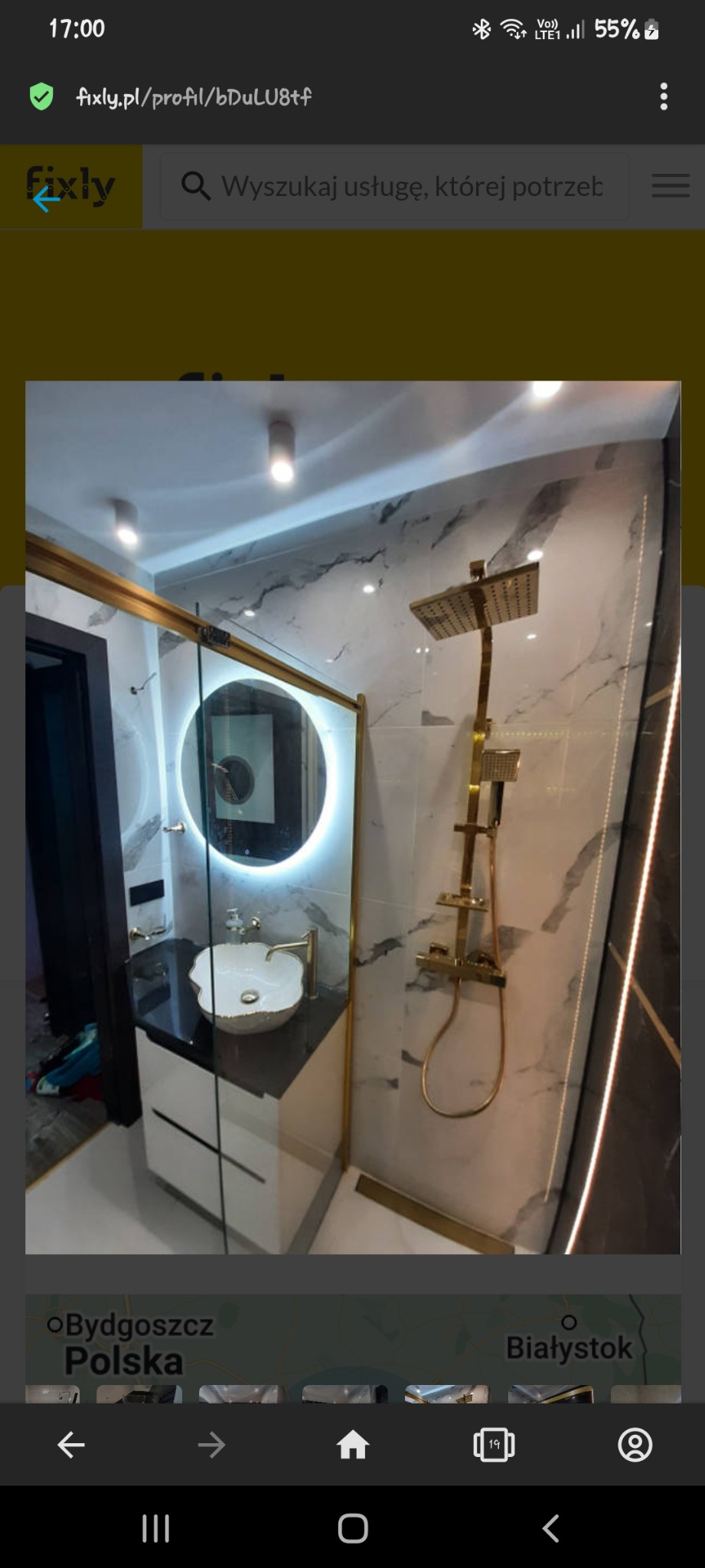 Luksusowa łazienka z kabiną prysznicową typu walk-in, marmurowymi płytami na ścianach, złotą armaturą, okrągłym lustrem z podświetleniem LED i umywalką w kształcie kwiatu.