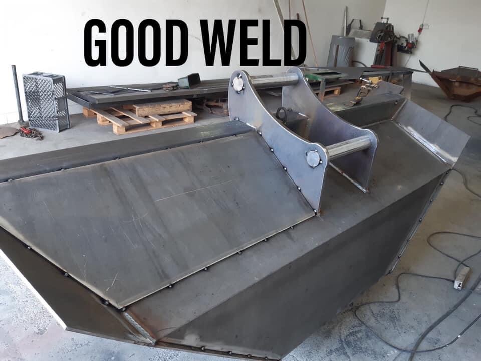 Spawana konstrukcja metalowa z widocznymi spawami, prawdopodobnie łyżka koparki, w warsztacie z narzędziami w tle.