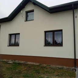 Branz-Bud - Ocieplona elewacja domu jednorodzinnego z brązowym cokołem, trzema oknami z firankami i numerem '6' na ścianie.