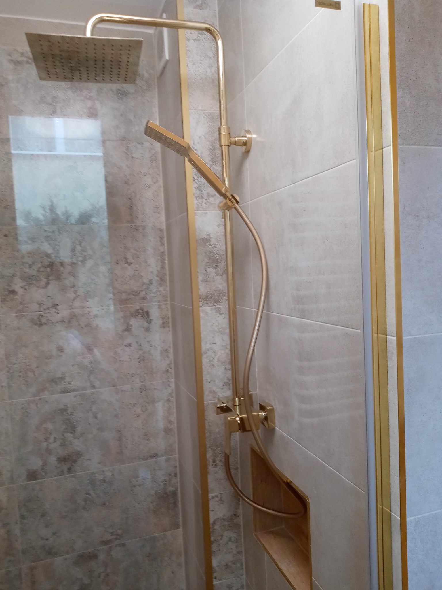 Złota armatura natryskowa z deszczownicą i wnęką w płytkach w wykończonej łazience w Piotrkowiu Trybunalskim.