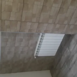 Ściana wyłożona beżową okładziną imitującą kamień, biały grzejnik i podłoga z szarych płytek imitujących drewno.