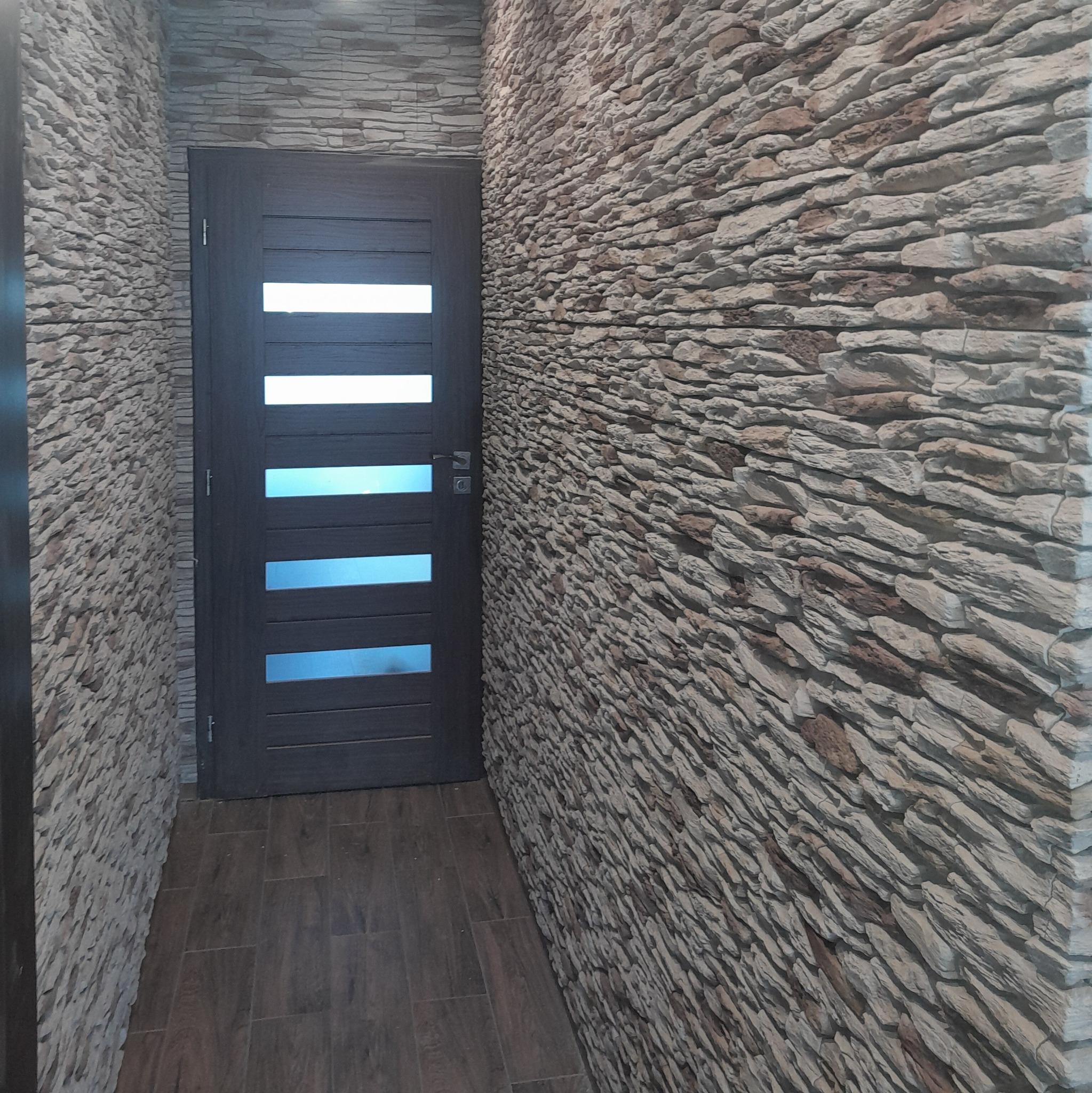 Wnętrze korytarza z dekoracyjną ścianą z kamienia i nowoczesnymi drzwiami z przeszkleniami.