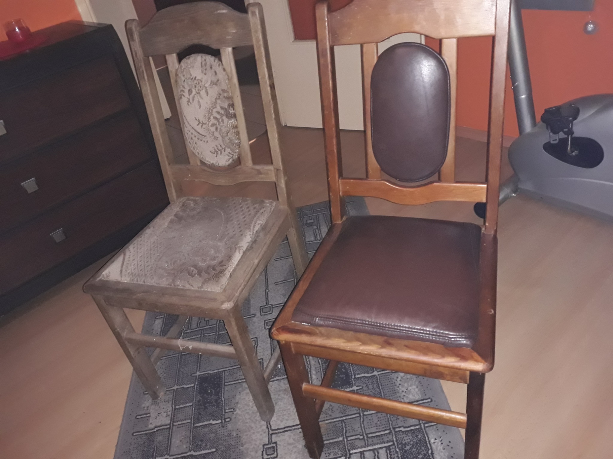 Dwa drewniane krzesła przed i po renowacji tapicerki. Po lewej krzesło z wytartą tapicerką, po prawej krzesło z nową, brązową skórą na siedzisku i oparciu. Widoczny ślad po szpachli na nodze...