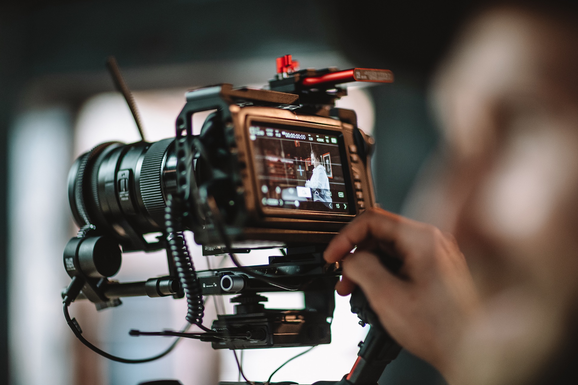 Profesjonalna kamera filmowa z obiektywem i monitorem, na którym widoczny jest nagrywany materiał, obsługiwana przez operatora