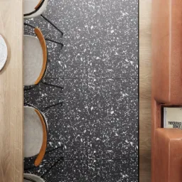 Widok z góry na fragment jadalni: drewniany stół z zastawą, krzesła z drewnianymi oparciami, podłoga z lastryko i fragment brązowej sofy z książką 'Longo Charcoal'.