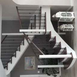 Nowoczesne schody z ciemnymi poręczami i białymi stopniami, oświetlenie ścienne, dekoracyjne lampiony i obraz na ścianie.