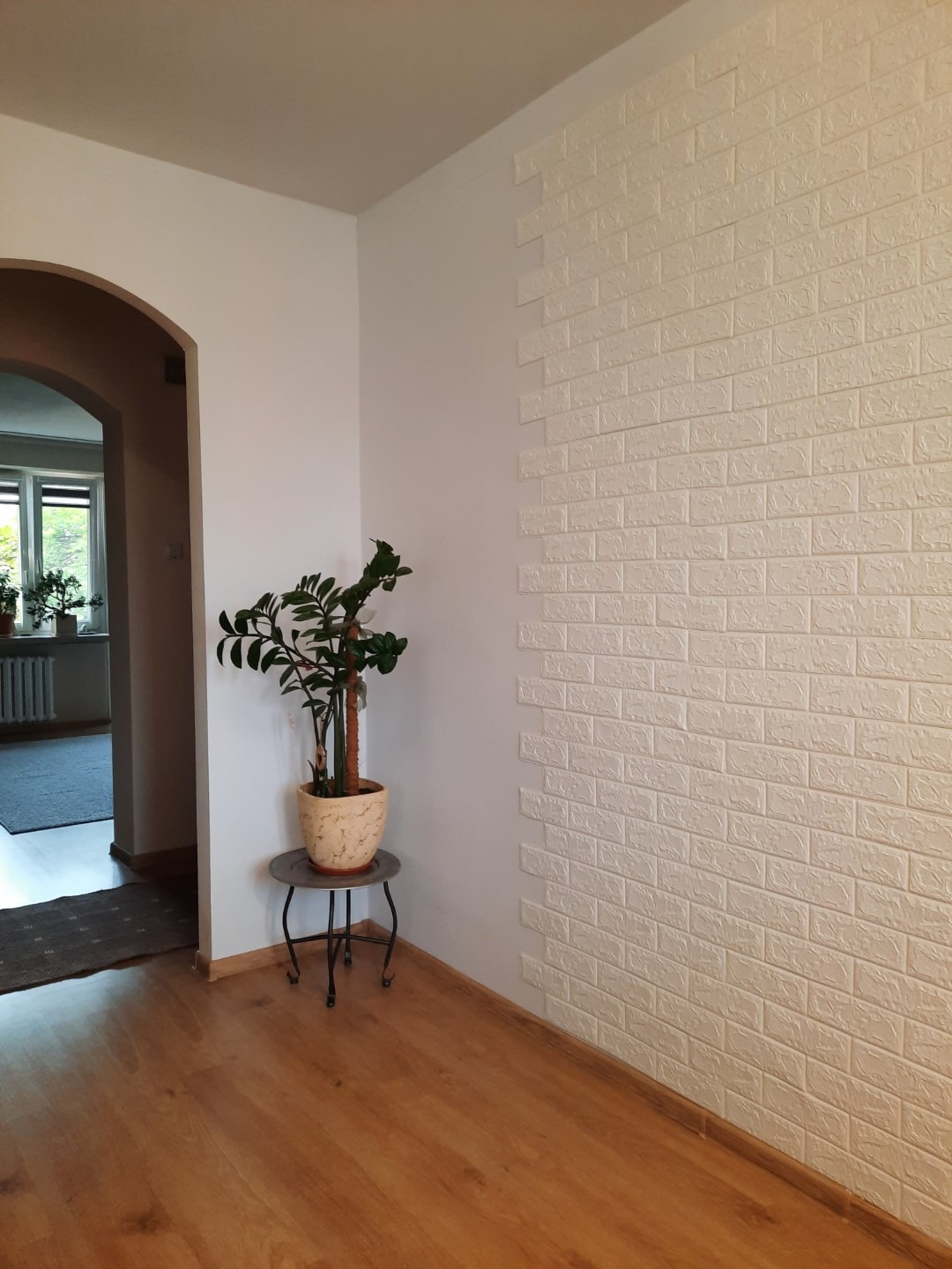 Fragment pokoju z panelami ściennymi imitującymi białą cegłę, ułożonymi schodkowo, z rośliną doniczkową na metalowym stoliku