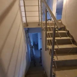 Montaż balustrady nierdzewnej na betonowych schodach w trakcie wykańczania, widoczna drabina i surowe ściany.