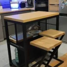 Stół barowy z blatem z jasnego drewna i czarną metalową konstrukcją, dwa pasujące stołki barowe z zygzakowatymi nogami, nowoczesna kuchnia w tle.